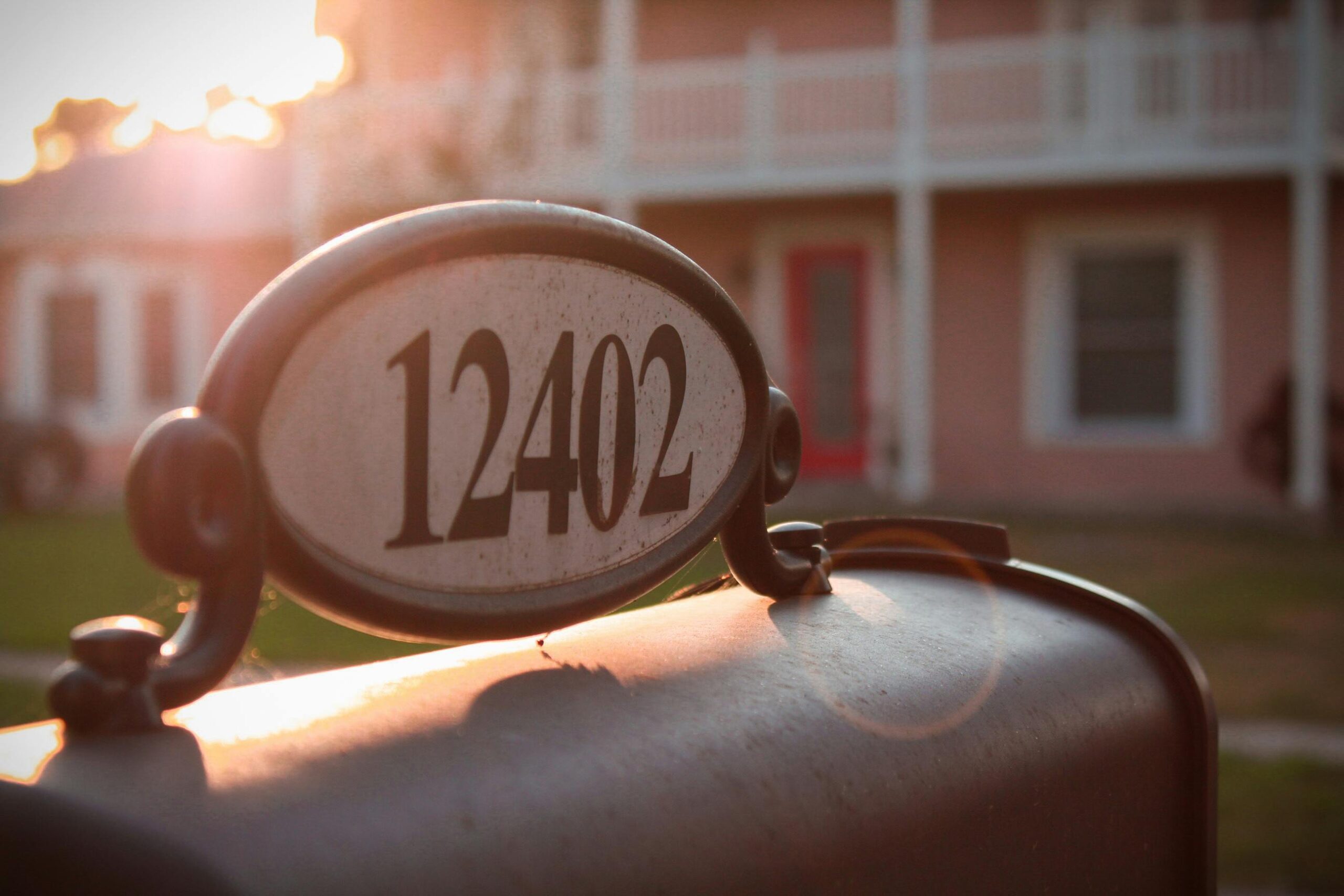 A vintage-style mailbox with the morning sun illuminating a house in the background.